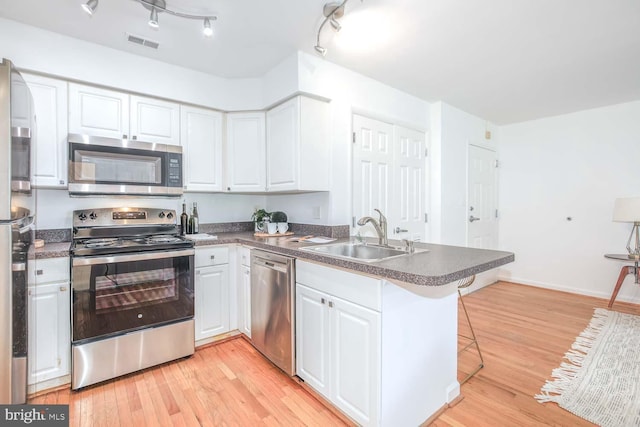 1308 Clifton St NW Unit 118, Washington, DC 20009 - kitchen featuring stainless steel appliances, a peninsula, white cabinetry, light wood-type flooring, and dark countertops