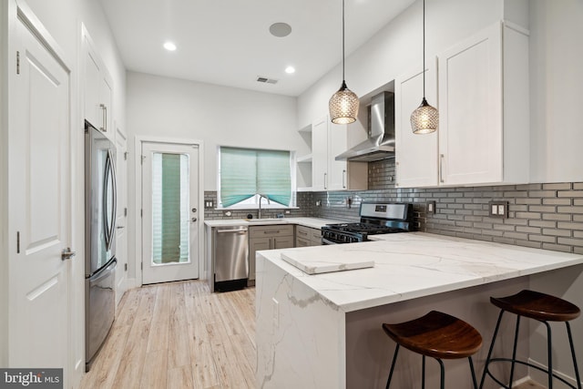 1448 N Myrtlewood St, Philadelphia, PA 19121 - kitchen featuring stainless steel appliances, wall chimney exhaust hood, a peninsula, light stone counters, and light wood finished floors