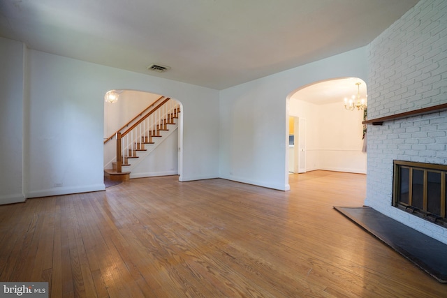 6339 Frederick Rd, Baltimore, MD 21228 - unfurnished living room with hardwood / wood-style floors, arched walkways, a brick fireplace, a chandelier, and stairway