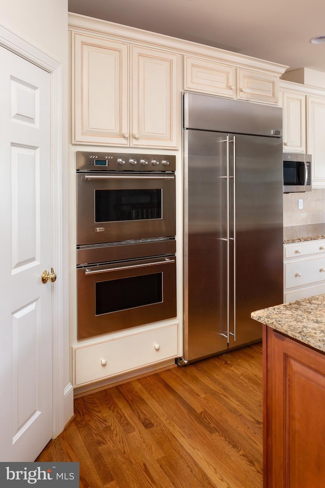 211 Twinings Ln, Wayne, PA 19087 - kitchen featuring appliances with stainless steel finishes, cream cabinetry, light stone countertops, light wood-type flooring, and decorative backsplash