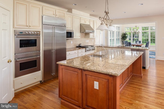 211 Twinings Ln, Wayne, PA 19087 - kitchen with appliances with stainless steel finishes, under cabinet range hood, cream cabinets, light wood-style flooring, and an island with sink