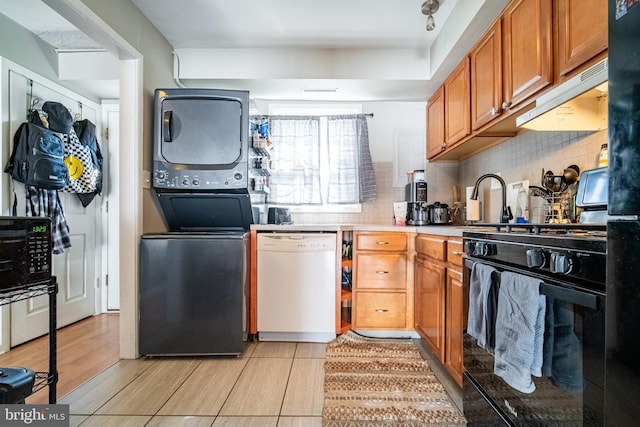 689 Colony Dr, York, PA 17404 - kitchen featuring white dishwasher, black gas stove, stacked washer / drying machine, under cabinet range hood, and brown cabinetry