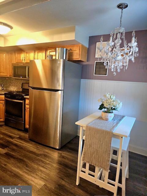 43 Briarcliffe Rd, Glenolden, PA 19036 - kitchen with stainless steel appliances, dark wood-style flooring, a chandelier, wainscoting, and tasteful backsplash