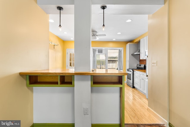 1148 S 12th St, Philadelphia, PA 19147 - kitchen featuring gas stove, white cabinetry, light wood-style floors, wall chimney range hood, and ceiling fan