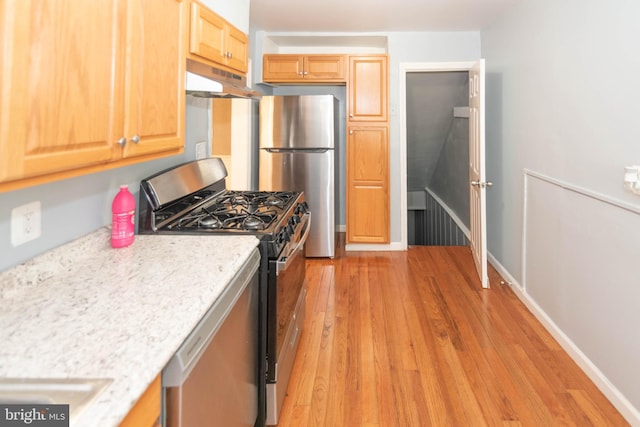 4917 Pembridge Ave, Baltimore, MD 21215 - kitchen with appliances with stainless steel finishes, under cabinet range hood, light wood finished floors, light brown cabinets, and light stone countertops