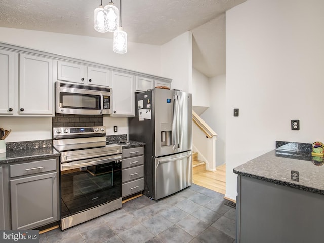 9907 Treetop Ln, Lanham, MD 20706 - kitchen featuring appliances with stainless steel finishes, gray cabinetry, vaulted ceiling, dark stone counters, and pendant lighting