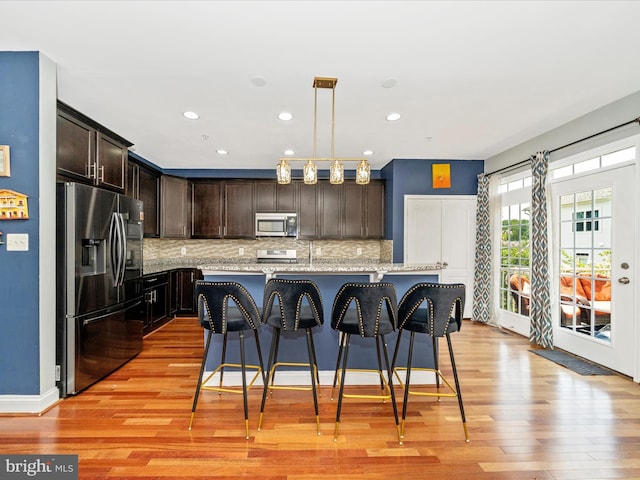 12404 Carriage Park Pl, Clarksburg, MD 20871 - kitchen with appliances with stainless steel finishes, dark brown cabinetry, light wood-style flooring, tasteful backsplash, and a kitchen bar