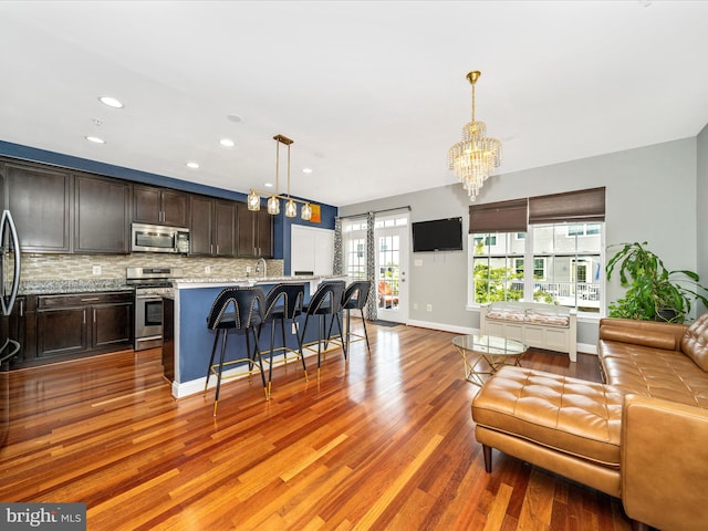 12404 Carriage Park Pl, Clarksburg, MD 20871 - kitchen with stainless steel appliances, open floor plan, a kitchen bar, backsplash, and wood finished floors