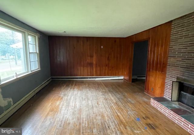 3001 Church Rd, Cherry Hill, NJ 08002 - unfurnished living room featuring hardwood / wood-style flooring, a brick fireplace, wooden walls, and baseboard heating