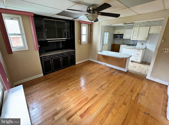 2805 Oakley Ave, Baltimore, MD 21215 - kitchen with stainless steel microwave, light wood-type flooring, a ceiling fan, a paneled ceiling, and white cabinets