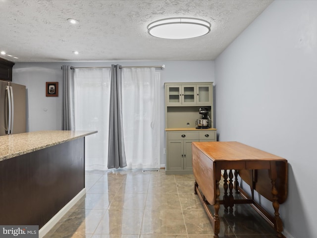 7313 Husky Ln, Springfield, VA 22151 - kitchen with a textured ceiling, freestanding refrigerator, light stone counters, glass insert cabinets, and recessed lighting