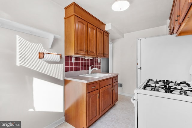 6344 Glenloch St, Philadelphia, PA 19135 - kitchen with white gas range oven, light countertops, decorative backsplash, brown cabinetry, and light tile patterned flooring