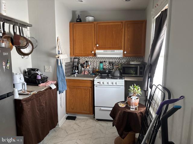 1329 N Dupont St, Wilmington, DE 19806 - kitchen featuring white range with gas cooktop, ventilation hood, stainless steel microwave, light countertops, and decorative backsplash