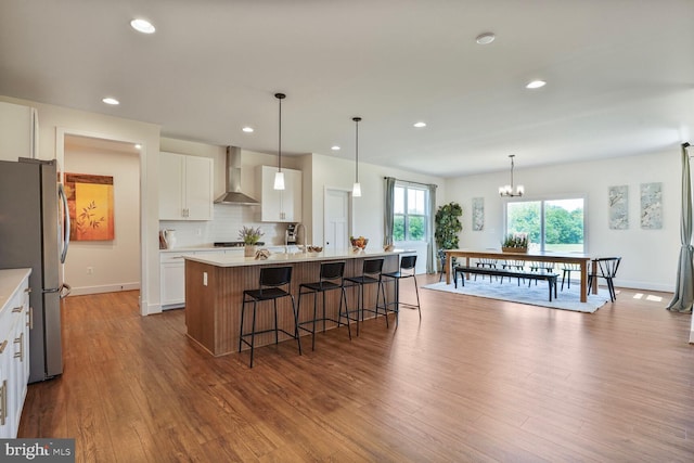 11100 Slate Landing Ln, Nokesville, VA 20181 - kitchen with wall chimney exhaust hood, freestanding refrigerator, a kitchen island with sink, dark wood-style flooring, and light countertops