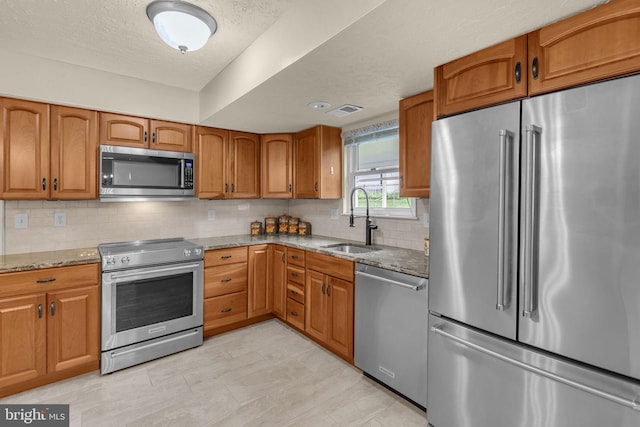 1848 Statesman Ct, Severn, MD 21144 - kitchen with appliances with stainless steel finishes, light stone countertops, brown cabinetry, decorative backsplash, and a textured ceiling