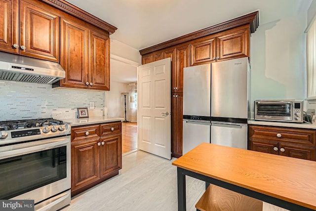 231 Candytuft Rd, Reisterstown, MD 21136 - kitchen featuring appliances with stainless steel finishes, light wood-style flooring, under cabinet range hood, tasteful backsplash, and light countertops