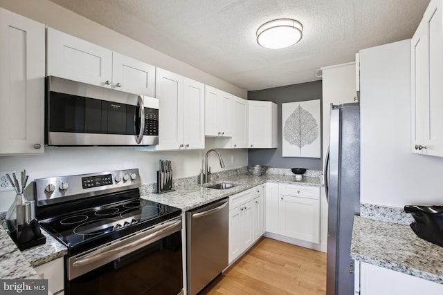 2059 Huntington Ave Unit 1406, Alexandria, VA 22303 - kitchen featuring appliances with stainless steel finishes, white cabinetry, light wood-style floors, a textured ceiling, and light stone countertops