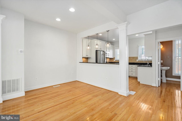 19 Yogurt Ln, Baltimore, MD 21231 - kitchen with dark countertops, freestanding refrigerator, light wood-type flooring, white cabinets, and decorative columns