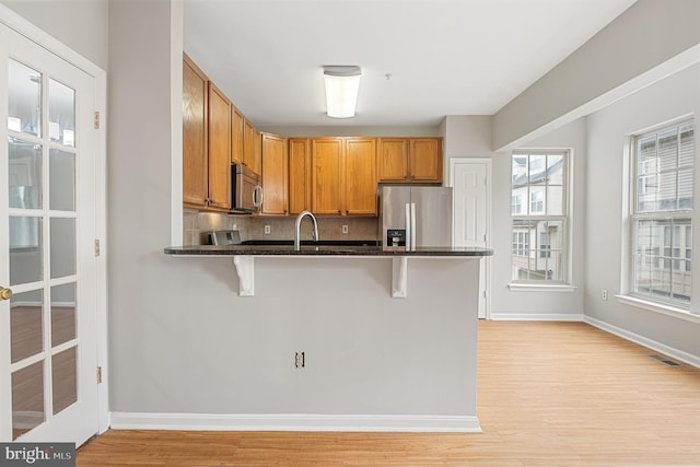 12119 Amber Ridge Cir, Germantown, MD 20876 - kitchen with stainless steel appliances, decorative backsplash, light wood-type flooring, a breakfast bar, and a peninsula