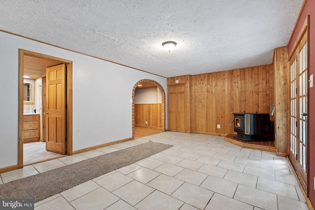 590 Vaught Dr, Front Royal, VA 22630 - unfurnished living room featuring a wood stove, wood walls, arched walkways, tile patterned floors, and a textured ceiling