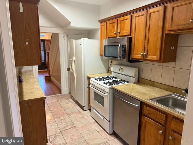 812 Emerson St NW, Washington, DC 20011 - kitchen featuring stainless steel appliances, brown cabinets, light countertops, and backsplash