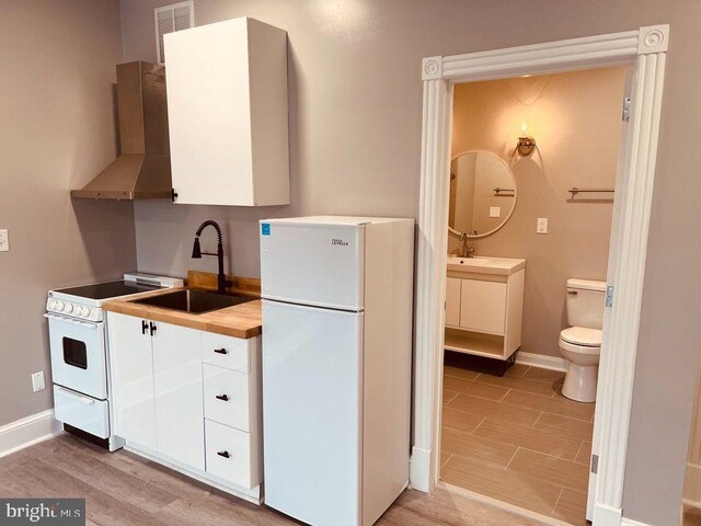 23 E Beverley St, Staunton, VA 24401 - kitchen featuring white appliances, wall chimney exhaust hood, white cabinets, light wood-style floors, and wood counters