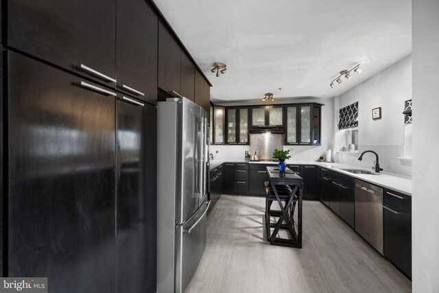 210 S High St, Baltimore, MD 21202 - kitchen with appliances with stainless steel finishes, light wood-style flooring, decorative backsplash, glass insert cabinets, and light countertops