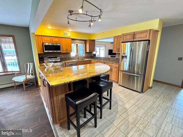 953 Capstan Dr, Forked River, NJ 08731 - kitchen with appliances with stainless steel finishes, a kitchen island, brown cabinetry, backsplash, and light stone countertops
