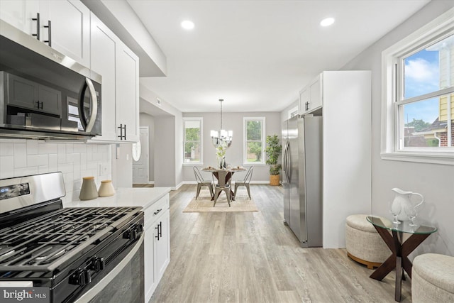 3912 Fernhill Ave, Baltimore, MD 21215 - kitchen featuring appliances with stainless steel finishes, light wood finished floors, a chandelier, tasteful backsplash, and white cabinetry