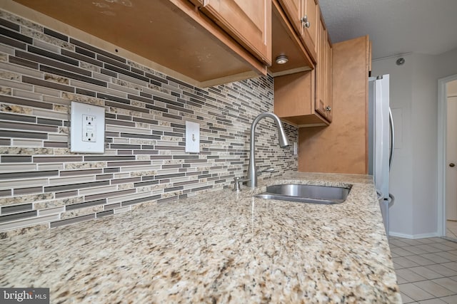 15100 Interlachen Dr Unit 4-207, Silver Spring, MD 20906 - kitchen with light tile patterned floors, backsplash, freestanding refrigerator, light stone counters, and brown cabinetry