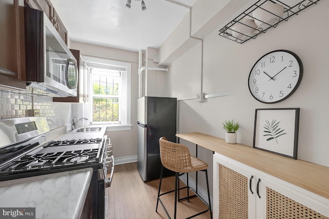 1954 Columbia Rd NW Unit 112, Washington, DC 20009 - kitchen featuring stainless steel appliances, light wood-style flooring, dark brown cabinetry, light countertops, and tasteful backsplash