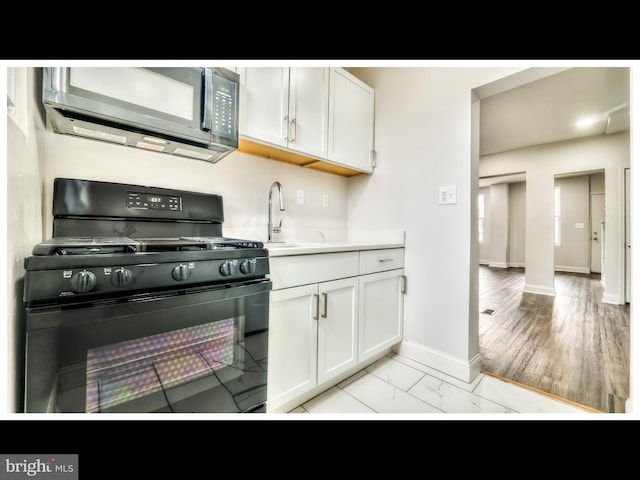 1206 Darley Ave, Baltimore, MD 21218 - kitchen featuring black gas range oven, stainless steel microwave, white cabinets, light countertops, and light marble finish floors