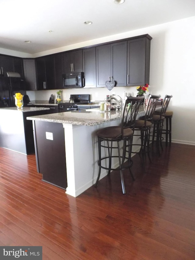 9545 Elizabeth Howe Ln, Owings Mills, MD 21117 - kitchen featuring black appliances, a peninsula, dark wood-type flooring, light stone counters, and a breakfast bar