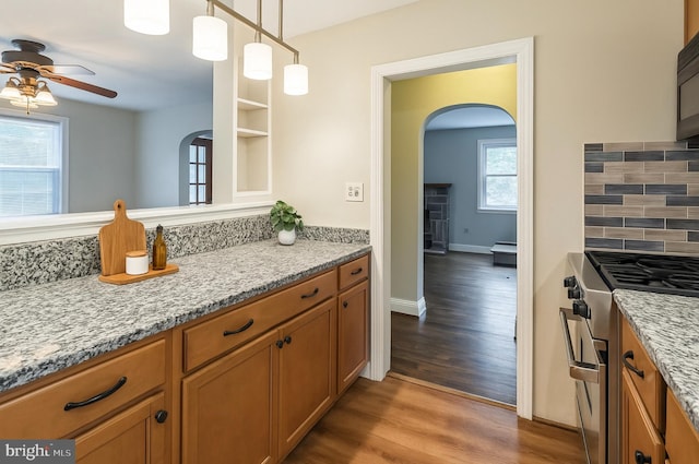 2504 Parkview Rd, Baltimore, MD 21207 - kitchen with gas range, arched walkways, a ceiling fan, brown cabinetry, and wood finished floors