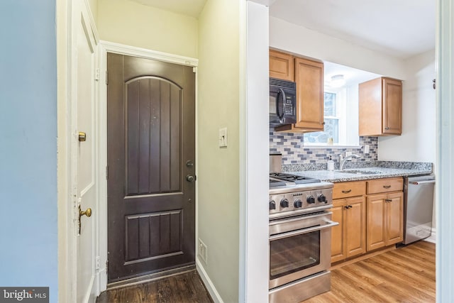 2504 Parkview Rd, Baltimore, MD 21207 - kitchen with appliances with stainless steel finishes, light wood-style floors, backsplash, light stone countertops, and brown cabinetry