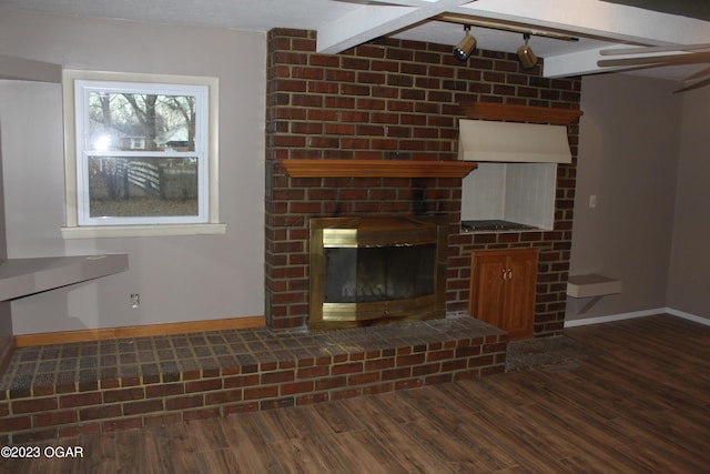 unfurnished living room featuring beam ceiling, a brick fireplace, track lighting, and dark wood-type flooring