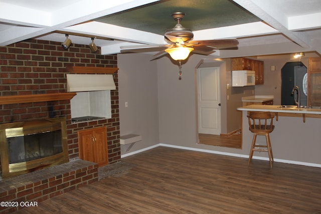 unfurnished living room featuring a brick fireplace, ceiling fan, sink, track lighting, and dark wood-type flooring