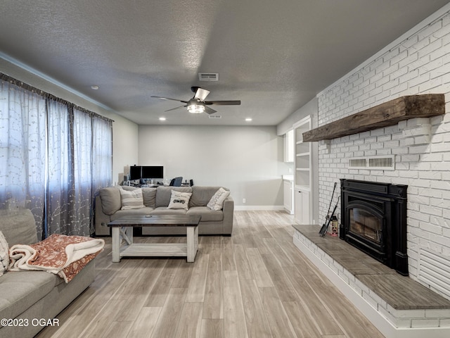 living room with a brick fireplace, a textured ceiling, ceiling fan, and light wood-type flooring