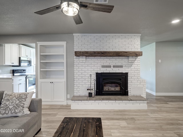 living room featuring ceiling fan, light wood-type flooring, a brick fireplace, and a textured ceiling