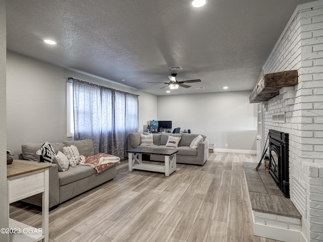 living room featuring light hardwood / wood-style floors, a textured ceiling, ceiling fan, and a brick fireplace