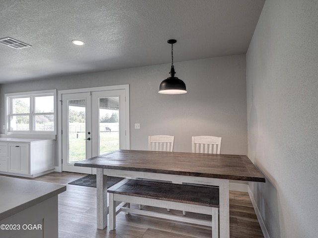 unfurnished dining area featuring a textured ceiling, light wood-type flooring, and french doors