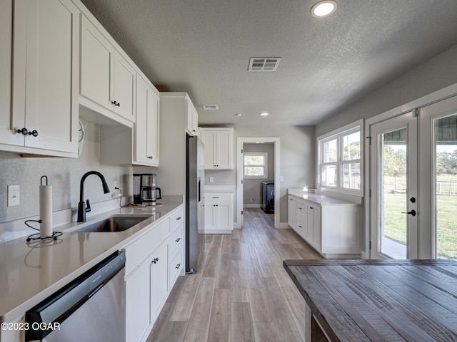 kitchen featuring sink, appliances with stainless steel finishes, white cabinets, light hardwood / wood-style floors, and a textured ceiling