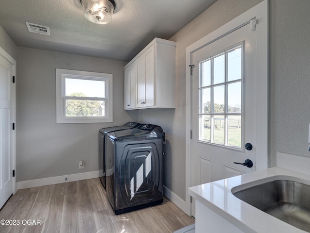 laundry room with sink, washer and clothes dryer, cabinets, a textured ceiling, and light wood-type flooring