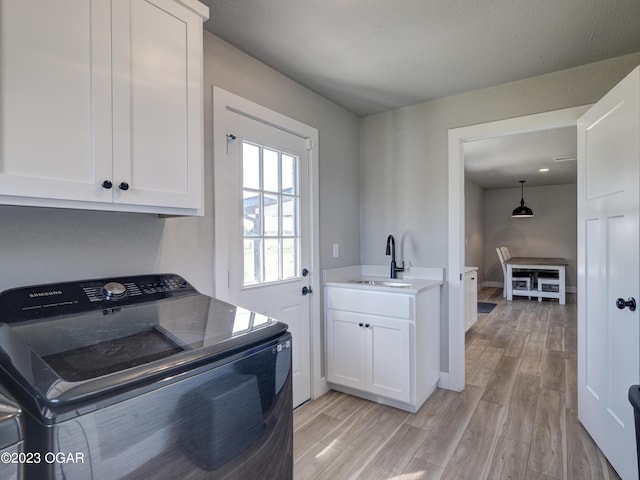 clothes washing area with light hardwood / wood-style floors, cabinets, sink, and washer and clothes dryer