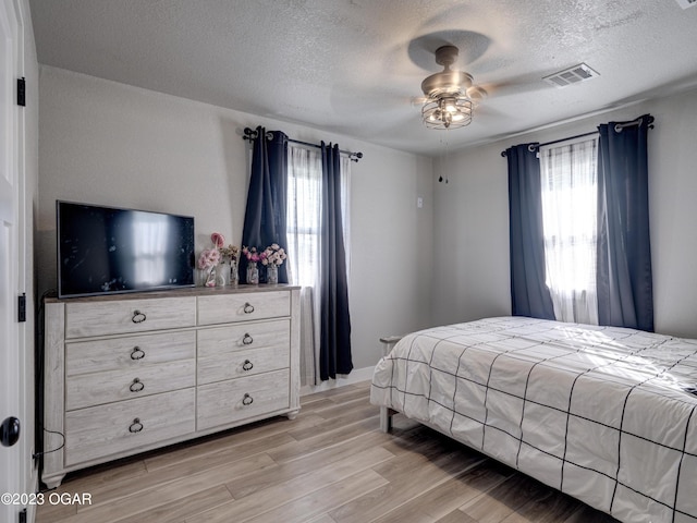 bedroom with ceiling fan, a textured ceiling, light wood-type flooring, and multiple windows