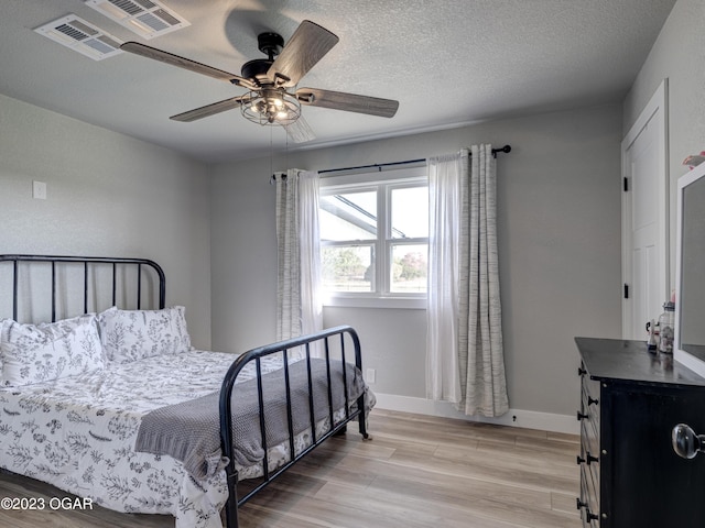 bedroom with a textured ceiling, ceiling fan, and light wood-type flooring