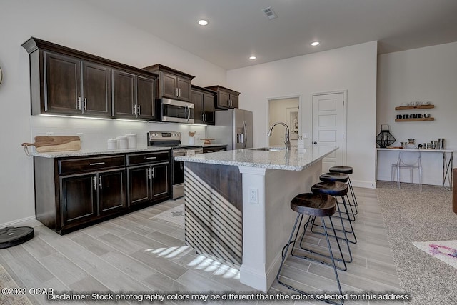 kitchen featuring light stone counters, sink, a breakfast bar area, dark brown cabinets, and stainless steel appliances