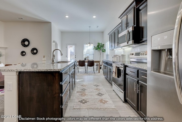 kitchen featuring a kitchen island with sink, decorative light fixtures, stainless steel appliances, sink, and tasteful backsplash