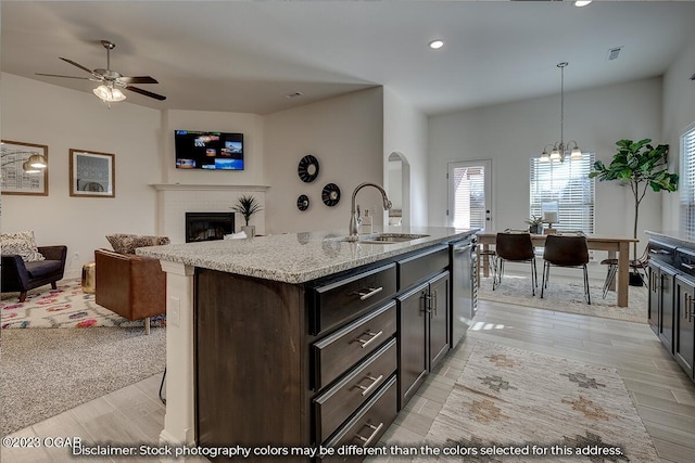 kitchen with pendant lighting, a kitchen island with sink, light stone countertops, ceiling fan with notable chandelier, and sink