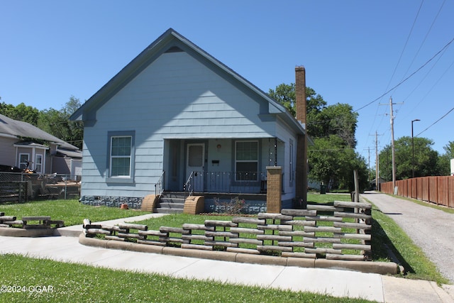 bungalow-style house with a front yard, covered porch, fence, and a chimney